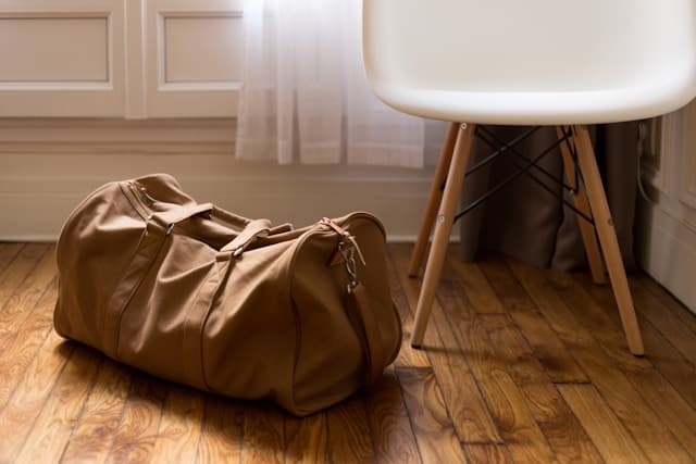 Tan leather duffle bag on warm wood floor — quiet, ready to go