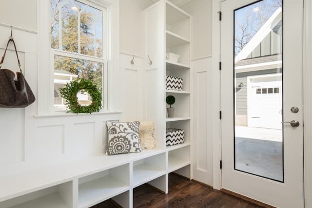 White built-in mudroom bench with cubbies, hooks, and a wreath in the window